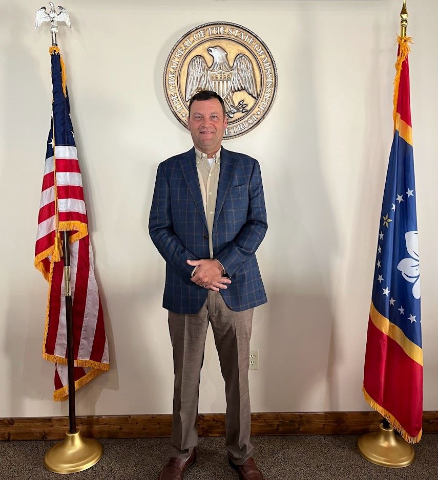 Man in front of state seal and flag