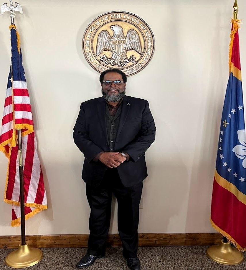Man in front of state seal and flag