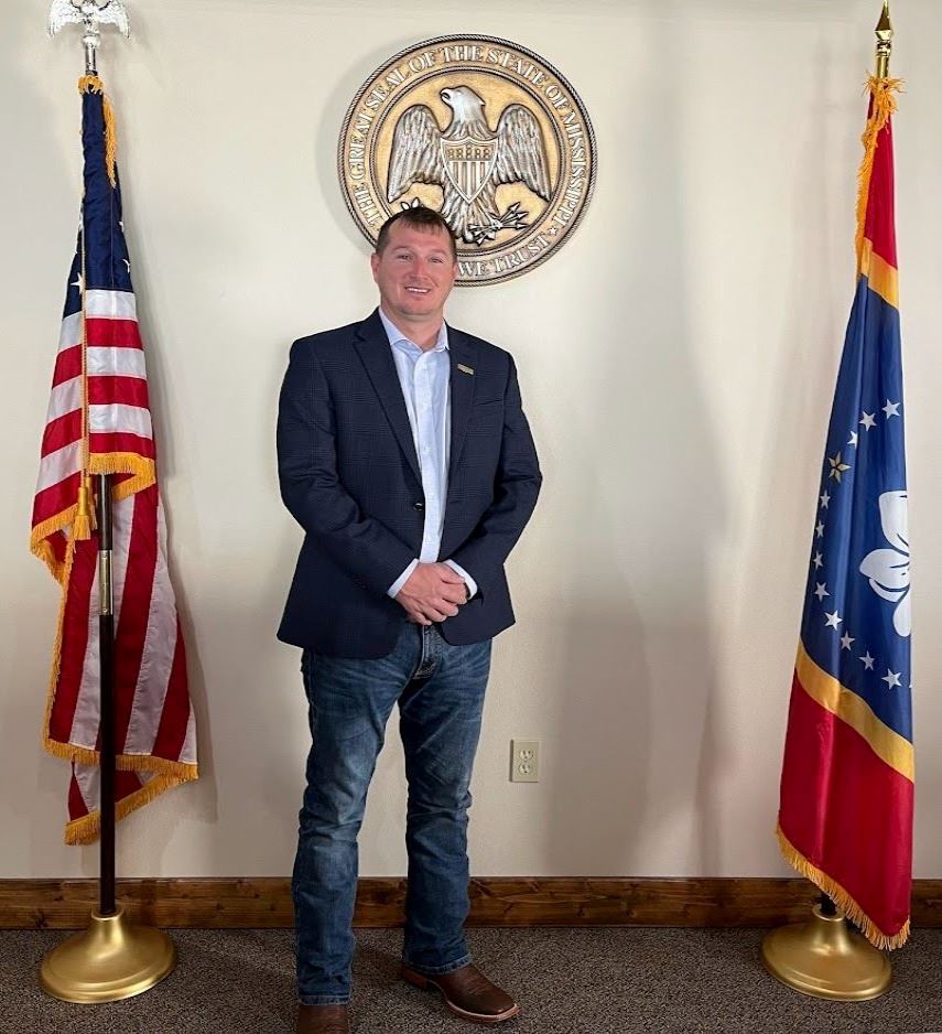 Man in front of state seal and flag