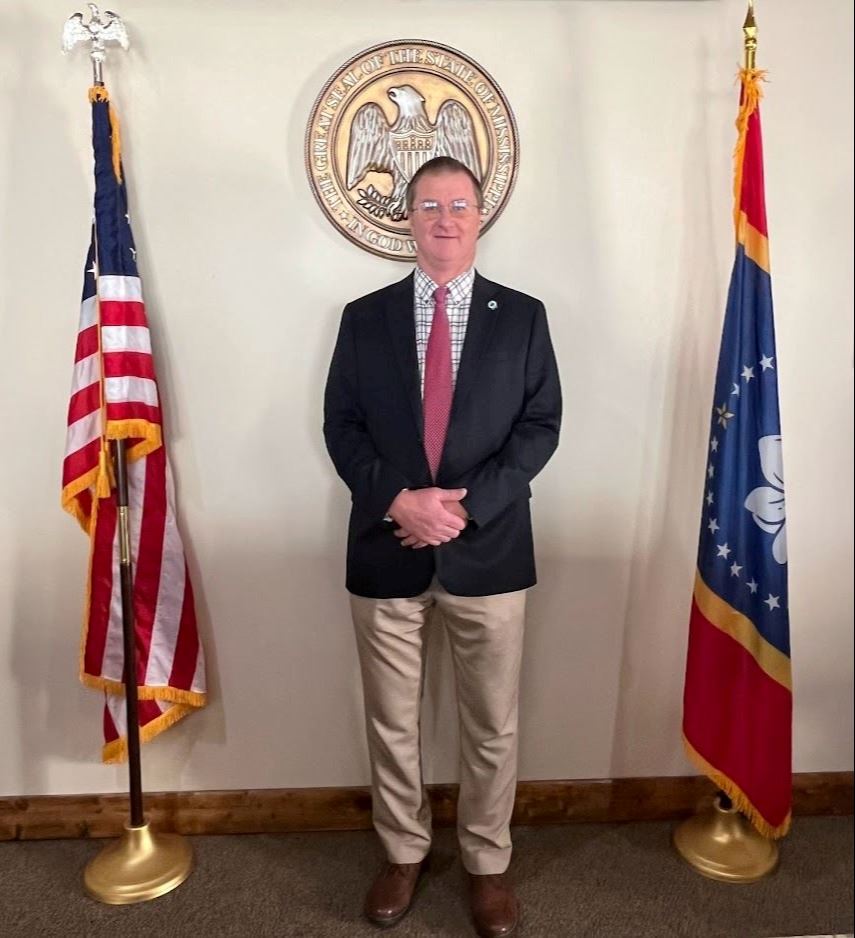 Man in front of state seal and flag
